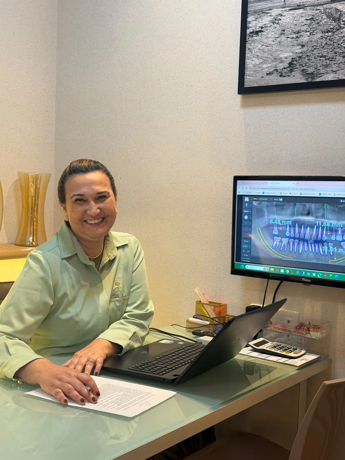 Dra. Cristiane Almeida sentada à mesa do consultório analisando o planejamento digital de um implante na tela