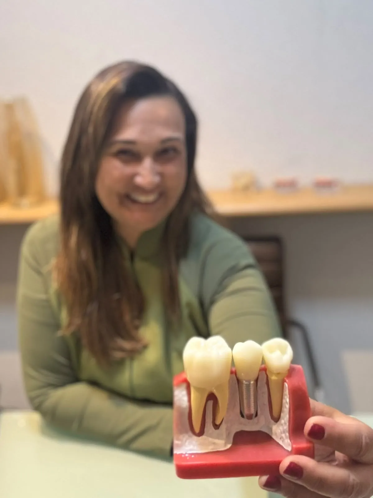 Dra. Cristiane Almeida segurando um modelo didático que mostra um implante dentário instalado no osso