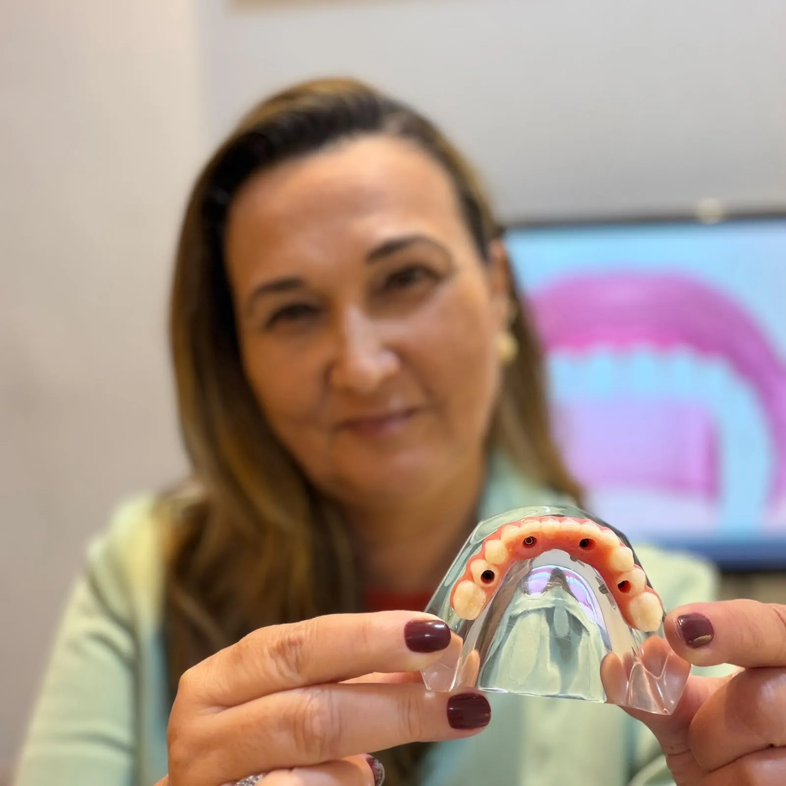 Dra. Cristiane Almeida segurando um modelo transparente de protocolo dentário com os pontos de fixação dos implantes